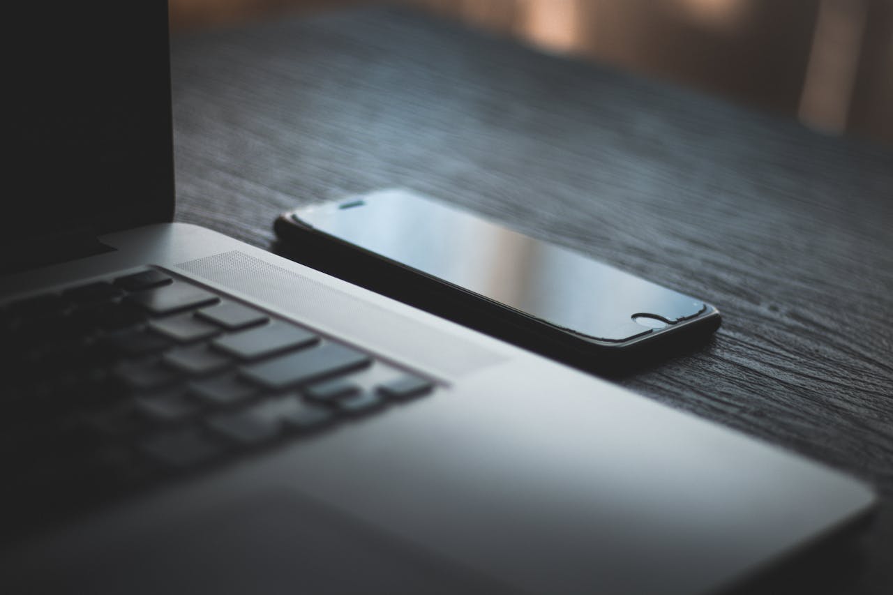 Modern laptop and smartphone on a textured wooden desk, capturing the essence of contemporary technology.